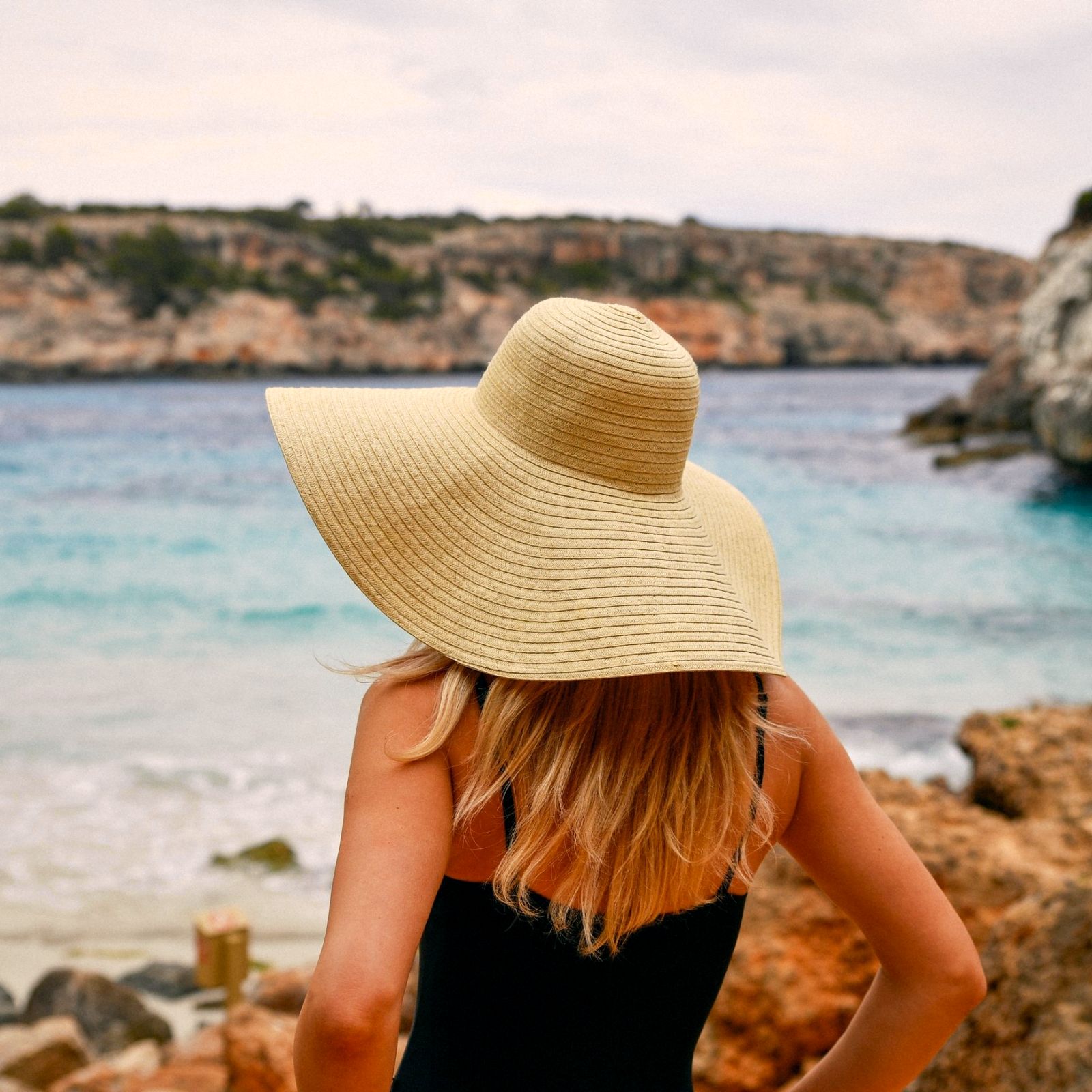 A woman in a wide straw hat looking over a turquoise cove