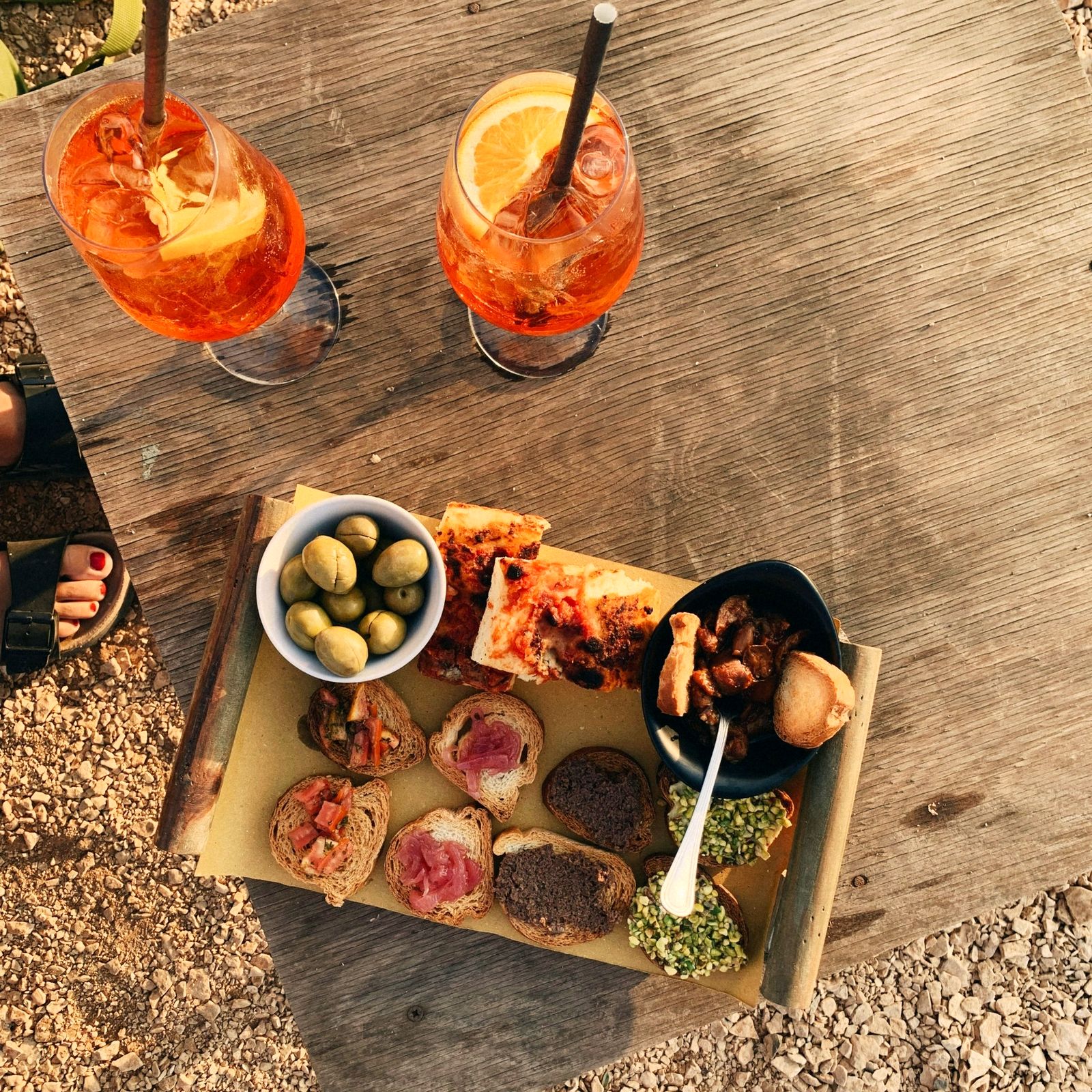 Two spritzes and a board of bruschetta and olives on a wooden table